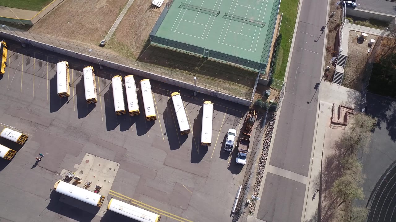 Top-down Hidden Lake, Colorado view with parked lorries arranged across the asphalt, tennis courts along the upper edge, and service vehicles near the right side, with no visible people.