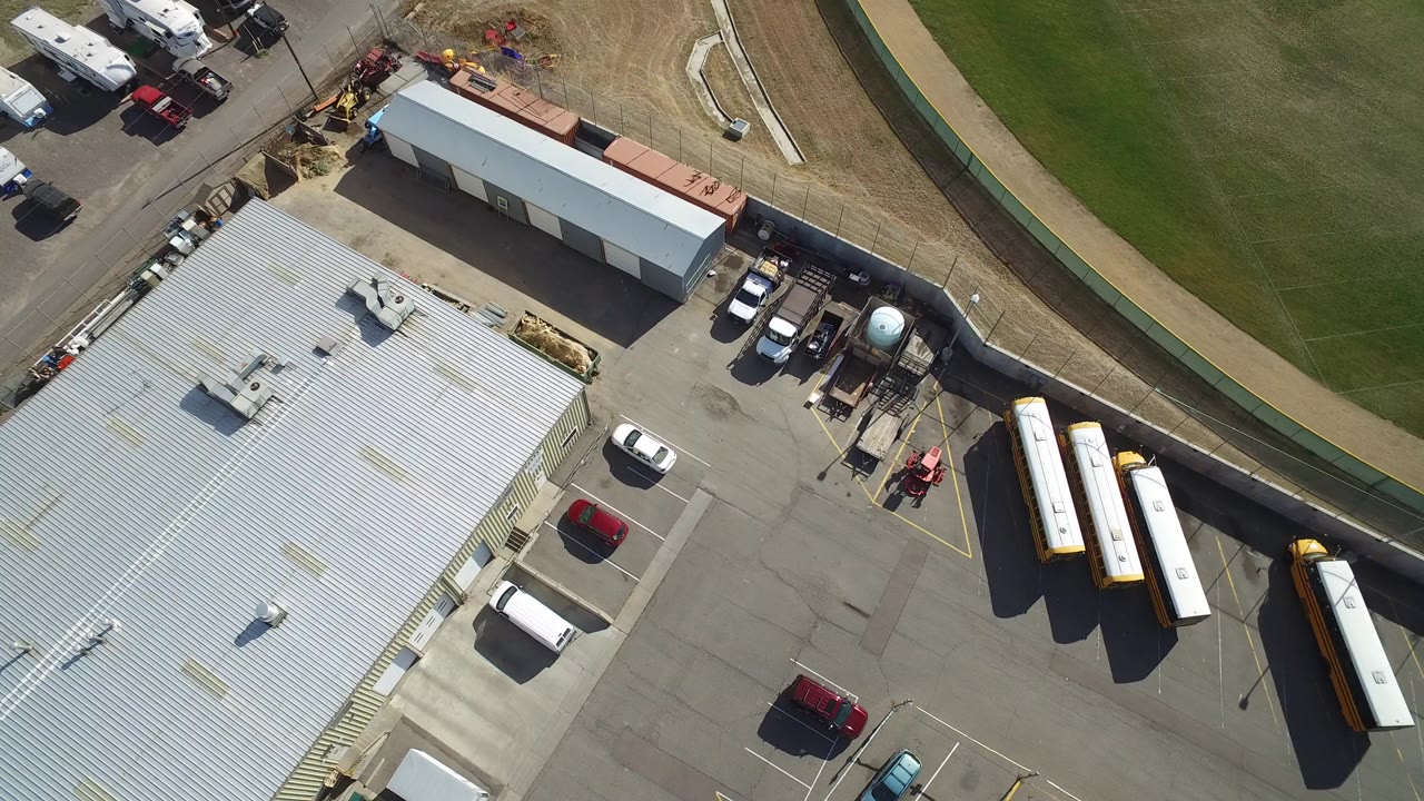 Overhead view of metal-roof industrial building and parked vehicles beside grass.