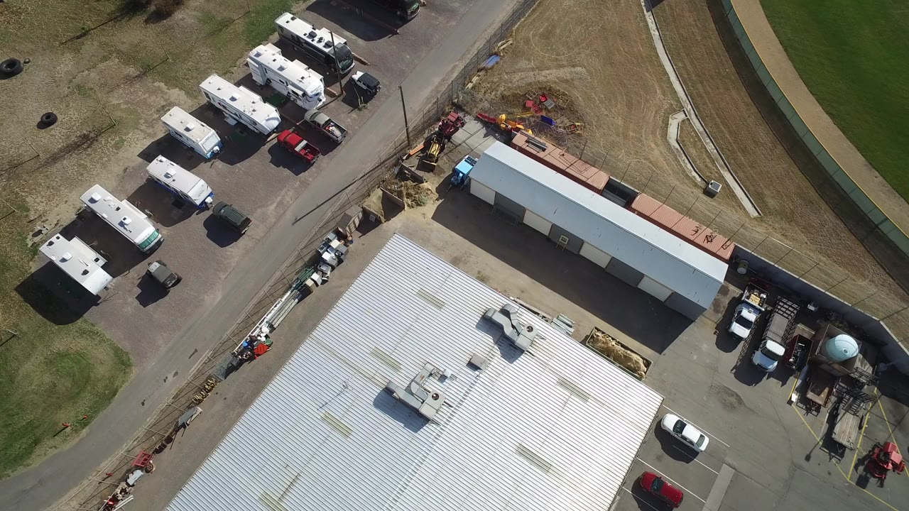 Overhead view of RVs and trucks parked near white-roofed buildings and grass.