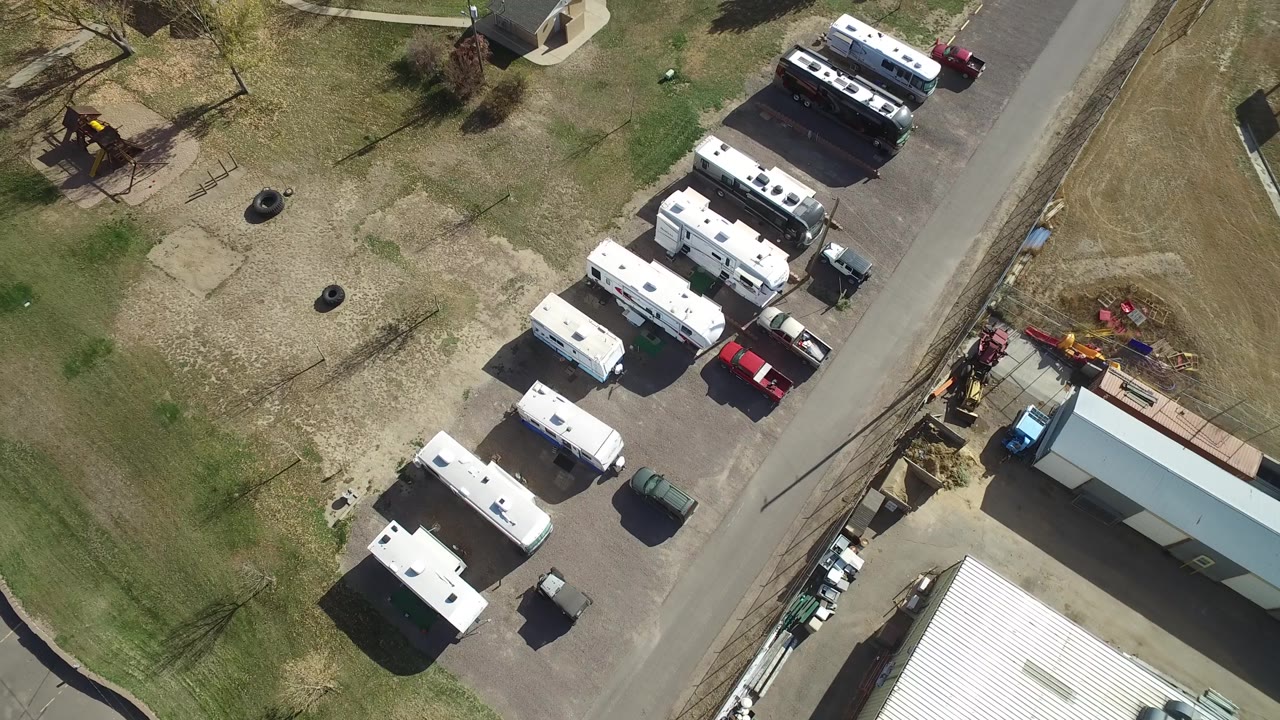 Drone-style overhead frame near Hidden Lake, Colorado with a diagonal road, several white trailers, red and dark parked vehicles, a playground area, and no visible people.