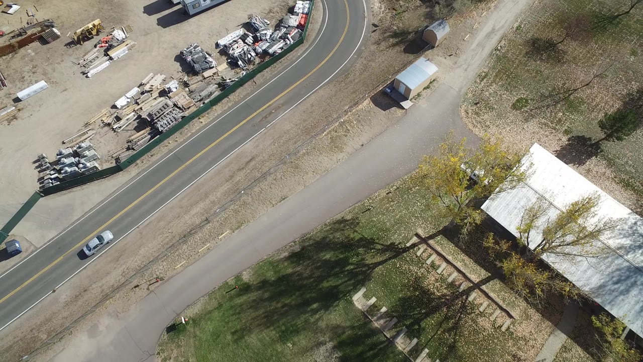 Aerial view of a road bend, fenced industrial yard, trees, and a building roof.