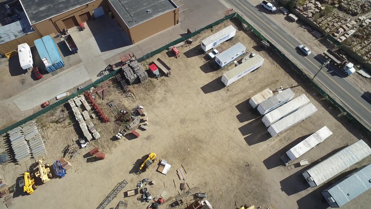 Overhead view of an industrial yard beside a road and tan building.