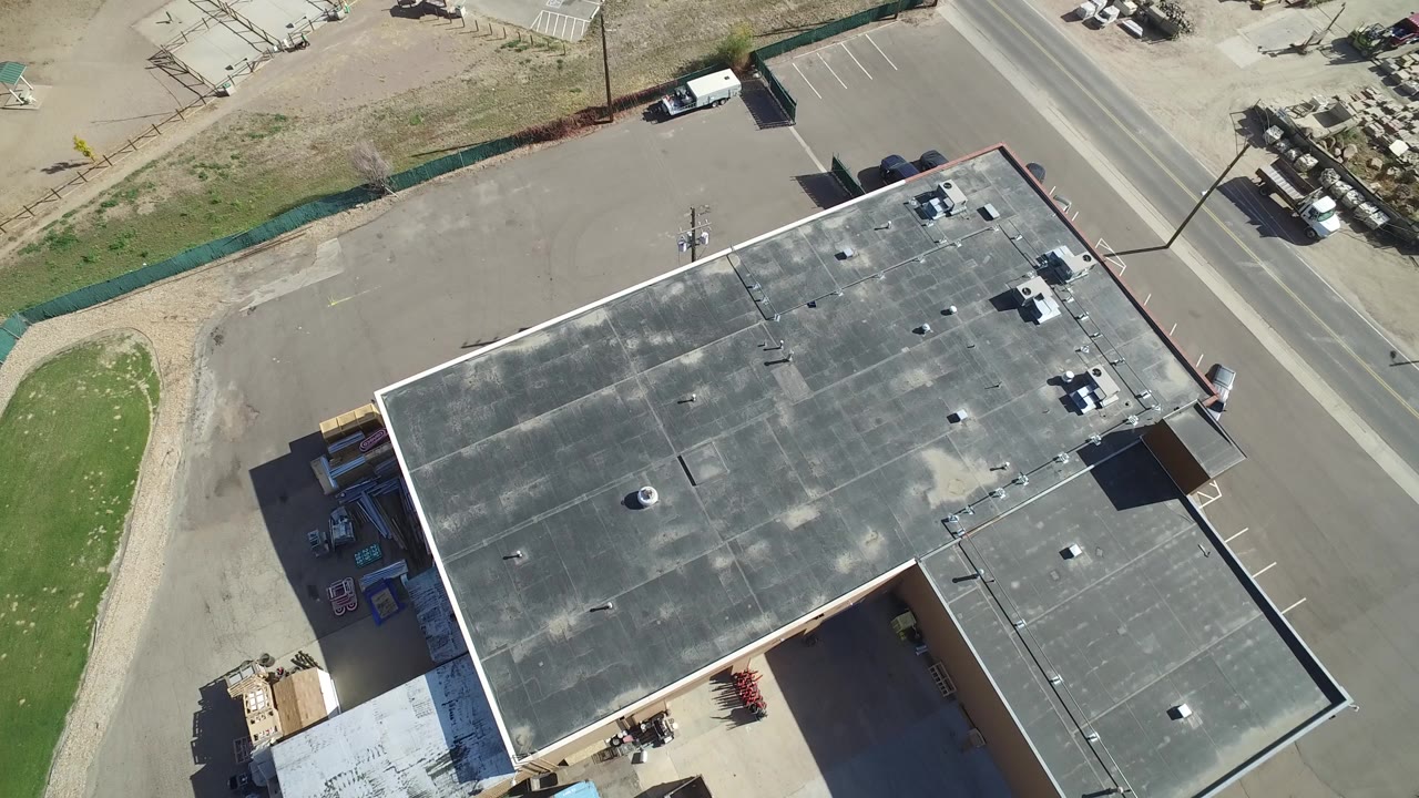 Overhead view of a large gray-roofed building beside pavement and a road.