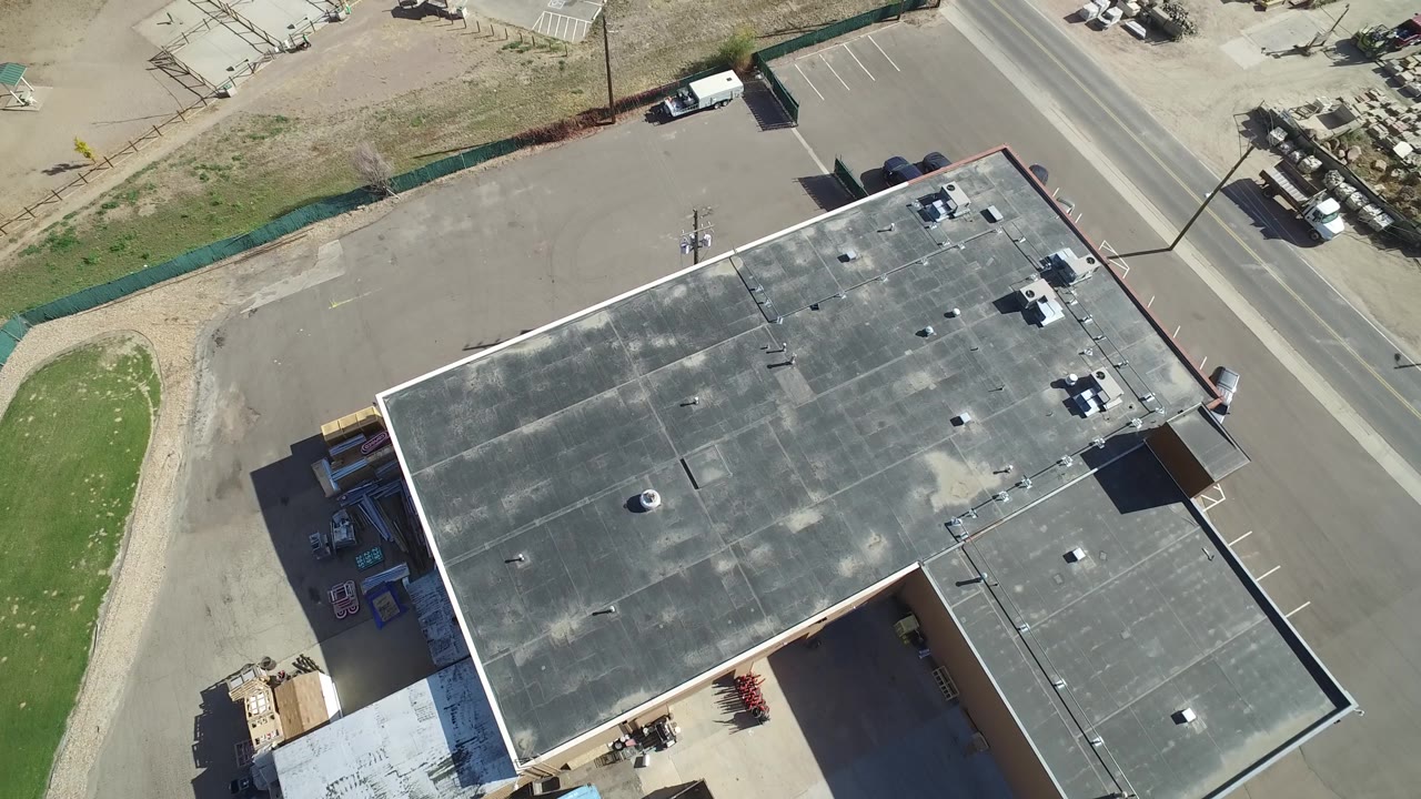 Aerial frame in Hidden Lake, Colorado with the gray roof centered, roof fixtures visible, open paved area to the side, a road at the top right, and no visible people.