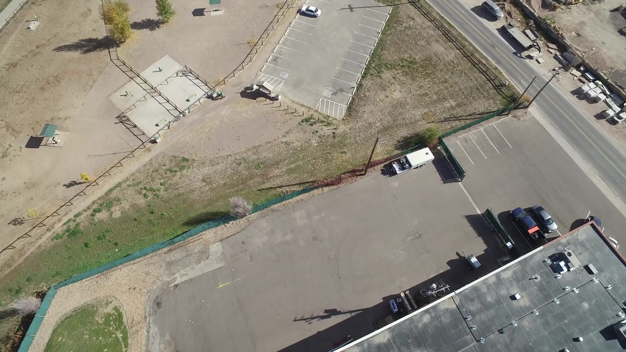 High aerial frame over Hidden Lake, Colorado showing a dirt lot, asphalt parking area, road edge, small structures, parked vehicles, and no visible people.