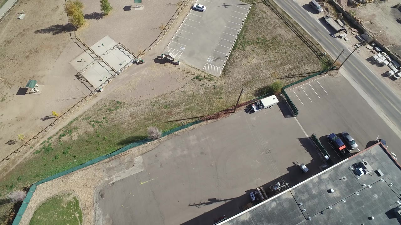 Aerial frame in Hidden Lake, Colorado with the road running along the upper right, striped parking stalls, dirt ground, fencing, small shelters, and no visible people.