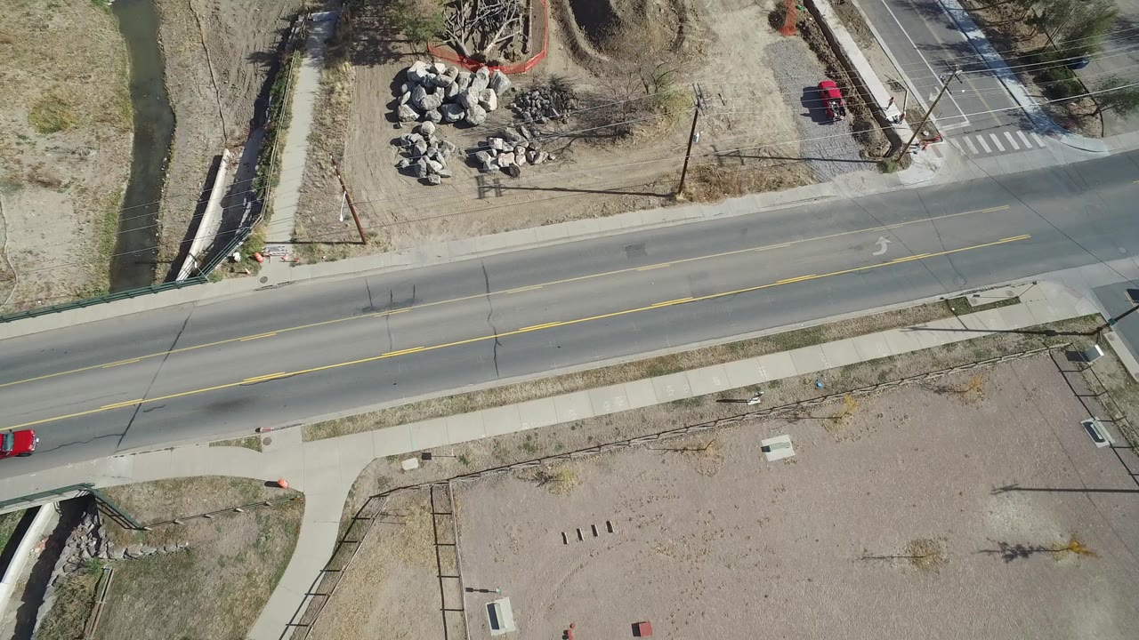 Aerial view in Hidden Lake, Colorado showing a two-lane road, sidewalk, narrow water channel, rock piles, and bare undeveloped ground with no visible people.