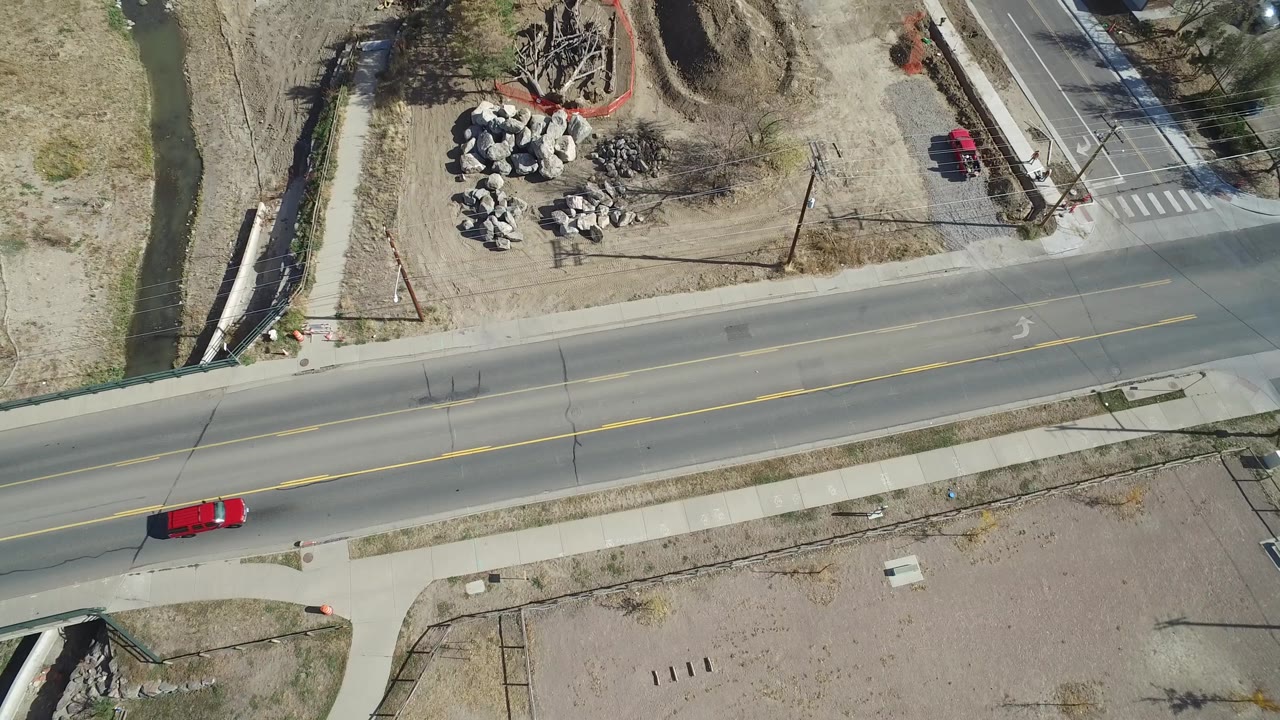 Red vehicle on road near a cross street and material piles.