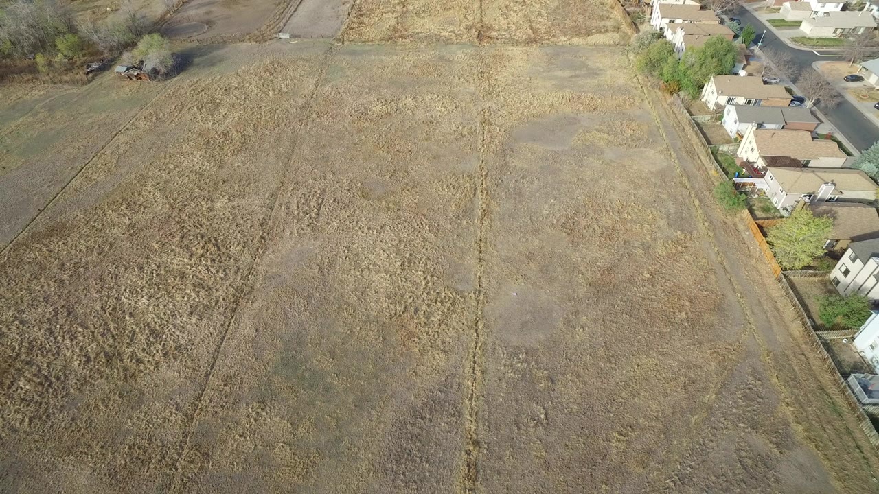 Aerial view of dry field beside houses and a road.