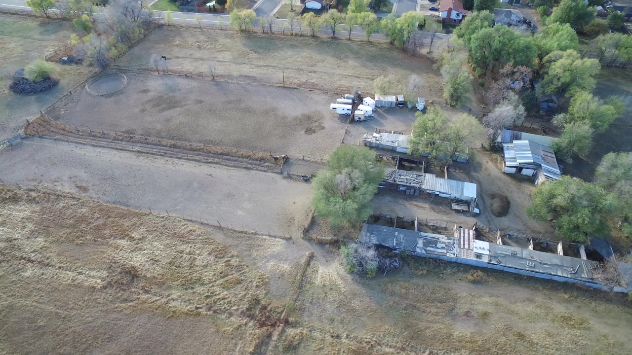 Aerial view of dry fields, fenced paddocks, farm buildings, trees, and nearby homes.