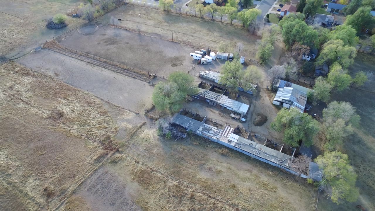 Aerial frame in Hidden Lake, Colorado with the long building cluster centered below dry open lots, trees along the right side, parked vehicles near the upper middle, and no visible people.