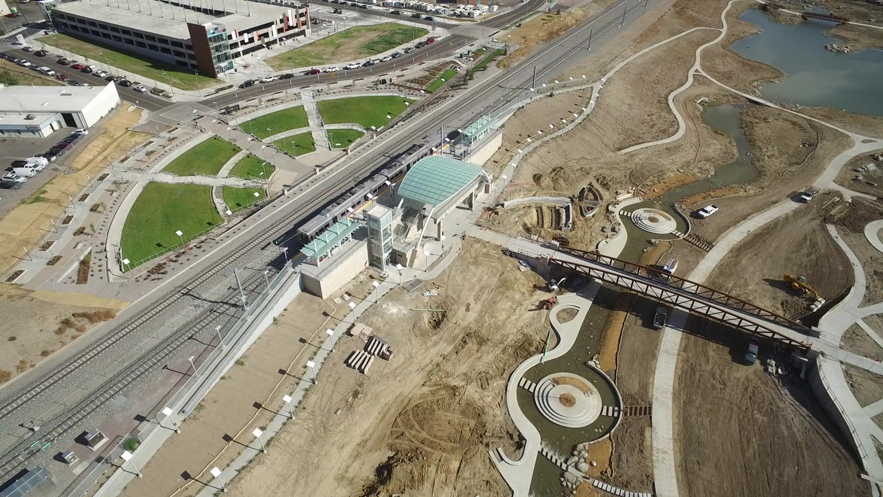 Aerial view of rail tracks, station canopy, dirt construction, paths, and water.