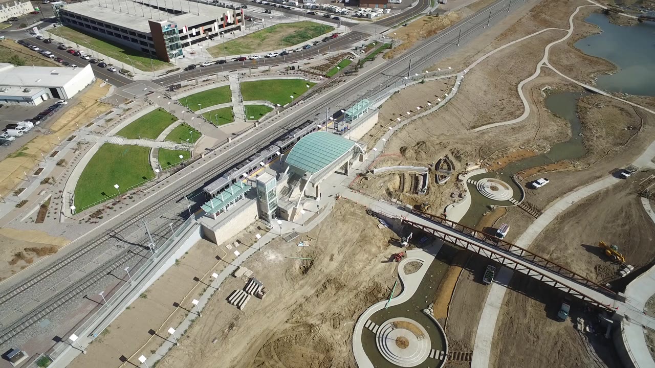 Hidden Lake, Colorado aerial frame with the rail station centered lower in view, parallel tracks crossing diagonally, roads above, ponds to the right, and no visible people.