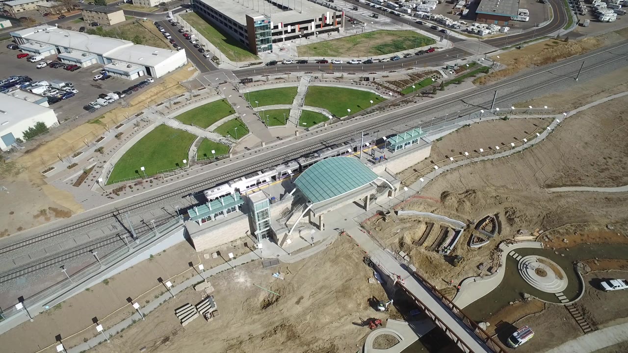 Overhead view of rail tracks, station canopy, paths, roads, and buildings.