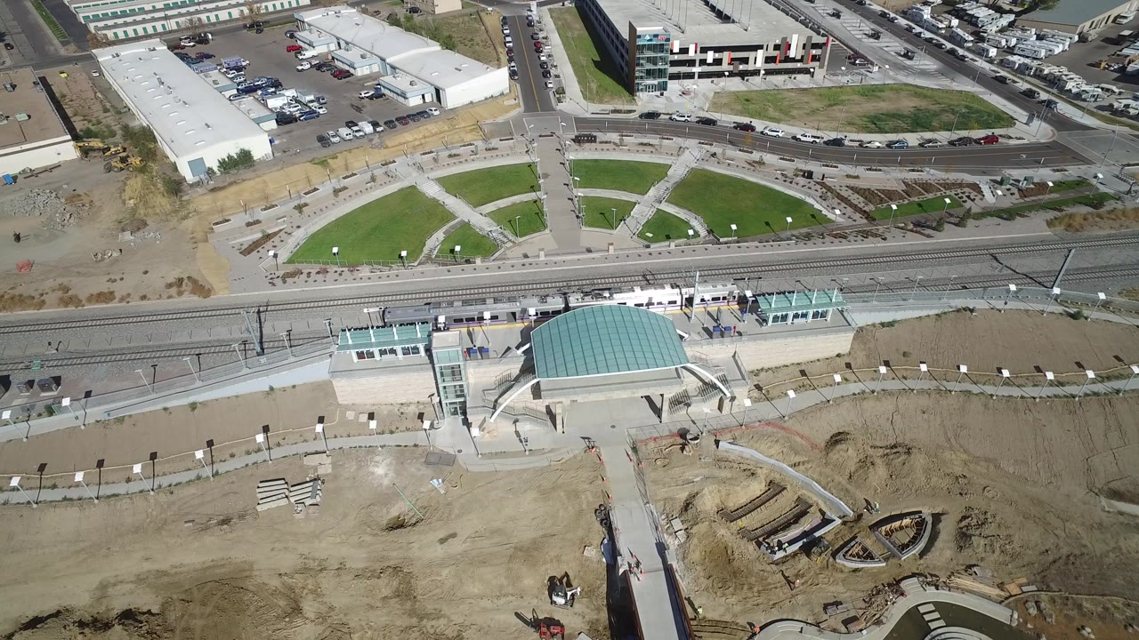 Aerial view of rail tracks, a glass-roofed station structure, roads, lawns, and construction dirt.