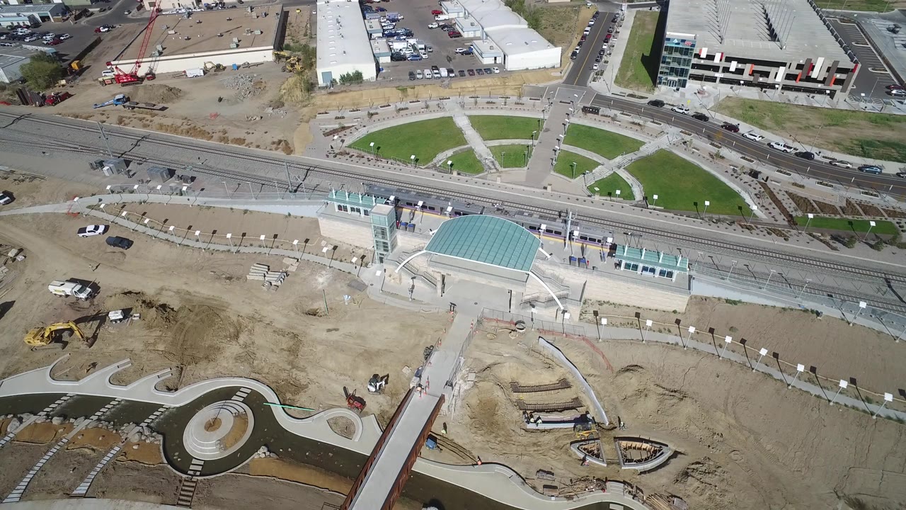 Aerial frame with circular plaza paths, rail tracks, roads, and construction equipment.