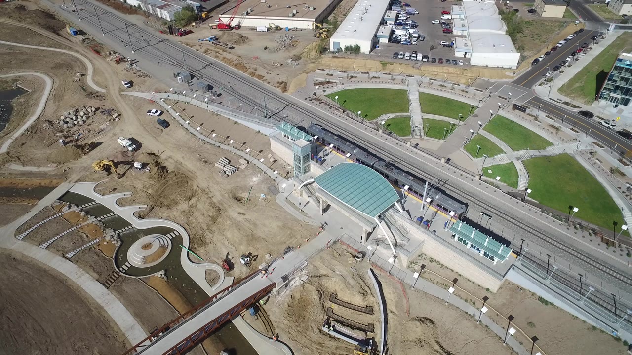 Overhead view of rail tracks, green lawns, roads, and a teal-roofed platform.