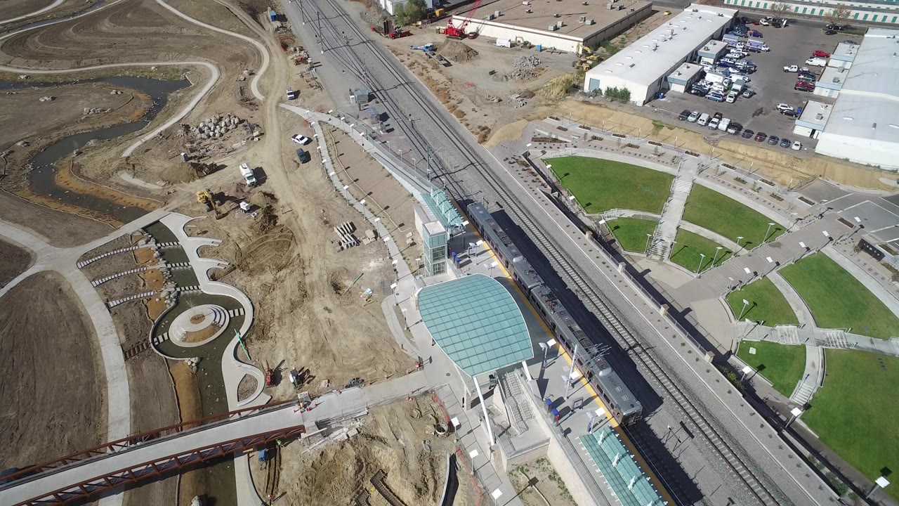 Aerial view in Hidden Lake, Colorado with the rail line near the center, curved paths and lawns to the right, construction earth to the left, parked cars, and no visible people.