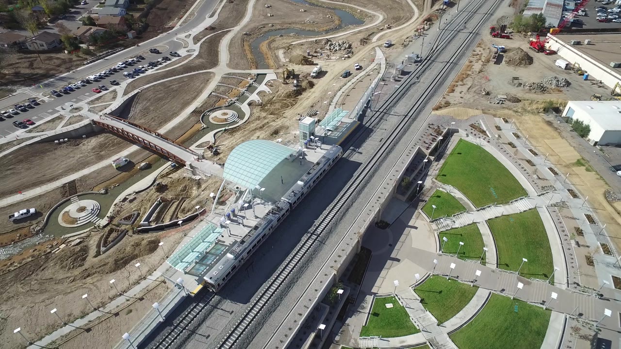 Drone-style overhead view of rail tracks, station structures, landscaped paths, and construction equipment.