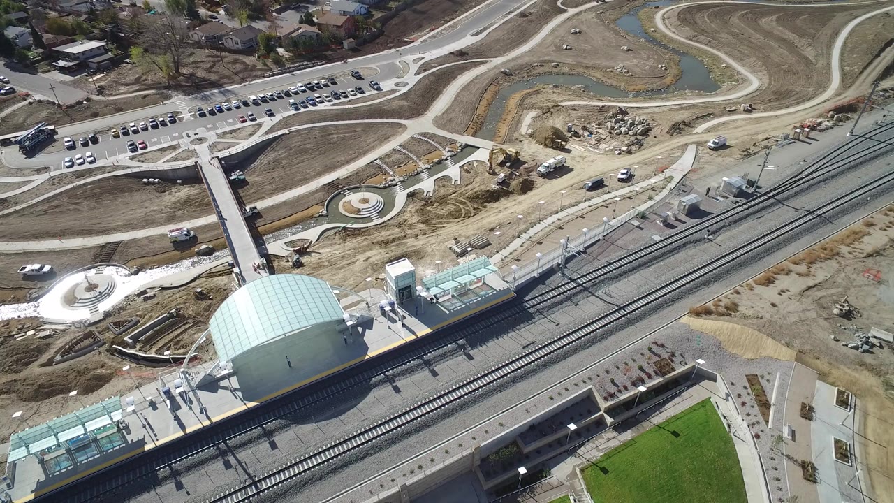 Aerial view of a rail station with tracks, paths, parked cars, and bare construction ground.