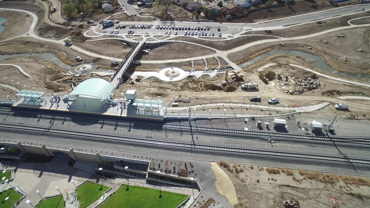 Aerial view of rail tracks, station platforms, parking, paths, ponds, and nearby roads.