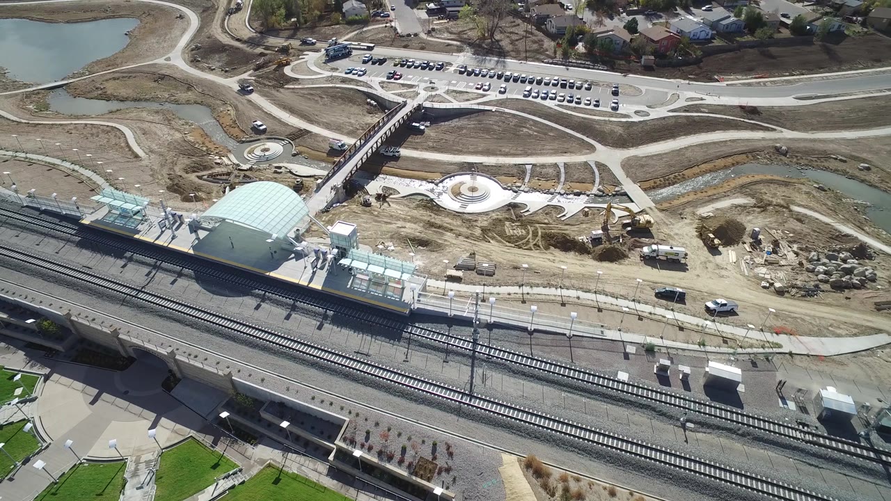 Aerial frame in Hidden Lake, Colorado keeps the rail tracks low in the view while the station canopy, glass-roofed sections, bridge, parking lot, ponds, and no visible people remain clear.