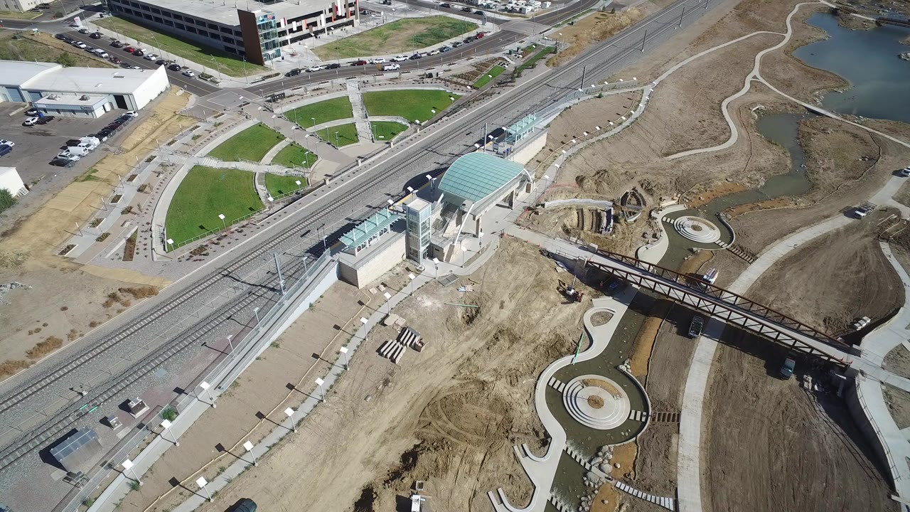 Aerial view of a modern building beside roads, rail tracks, paths, and graded earth.