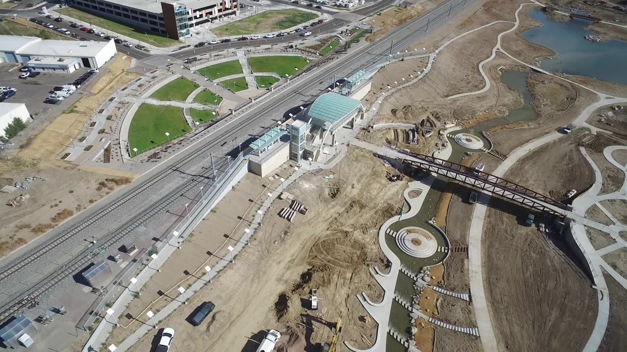 Aerial view of rail tracks, a station canopy, curving paths, construction dirt, and ponds.