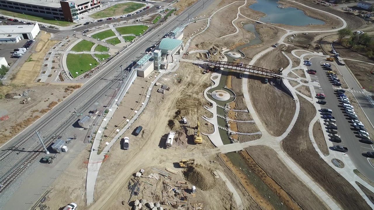 Overhead view of paths, parking rows, rail tracks, bridge, and construction materials.