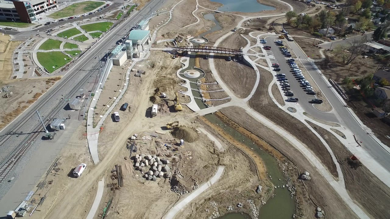 Aerial view of roads, rail tracks, paths, parked cars, water, and bare construction ground.
