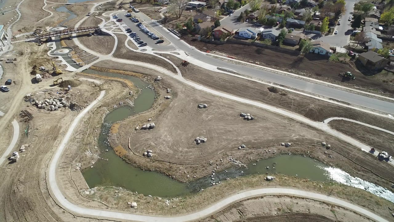 Aerial view of a curved pond, dirt lots, roads, and houses.