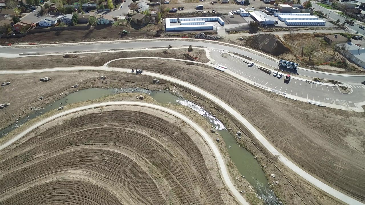 Aerial view of curved dirt markings, a pale path, drainage water, roads, vehicles, and nearby buildings.