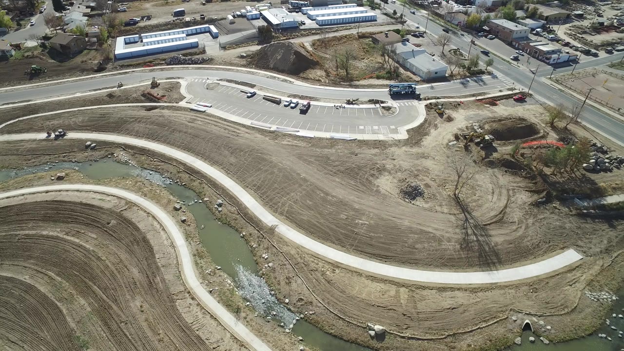 Aerial view of a curving path beside a muddy canal and graded park land.