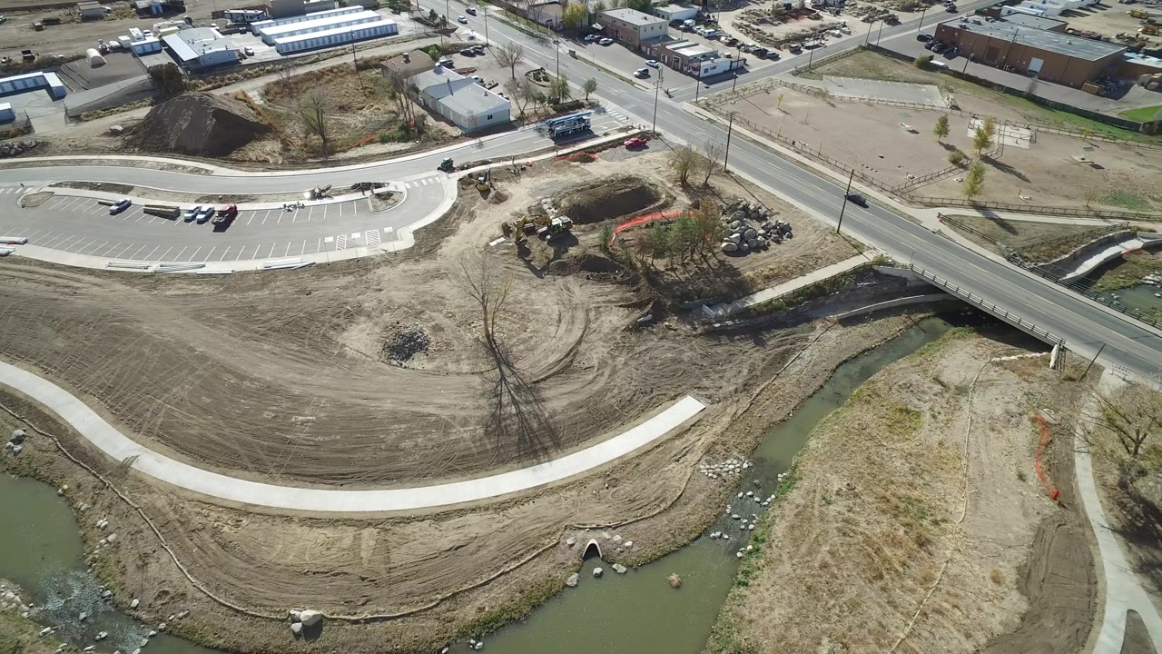 Aerial view of a road bridge, dirt lots, creek, and curved concrete path.