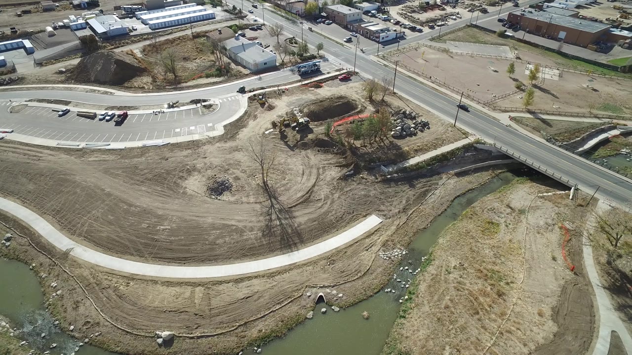 Hidden Lake, Colorado appears from a high drone angle with the road running diagonally, the creek channel below, a small parking area, dirt work, and low buildings in the background.