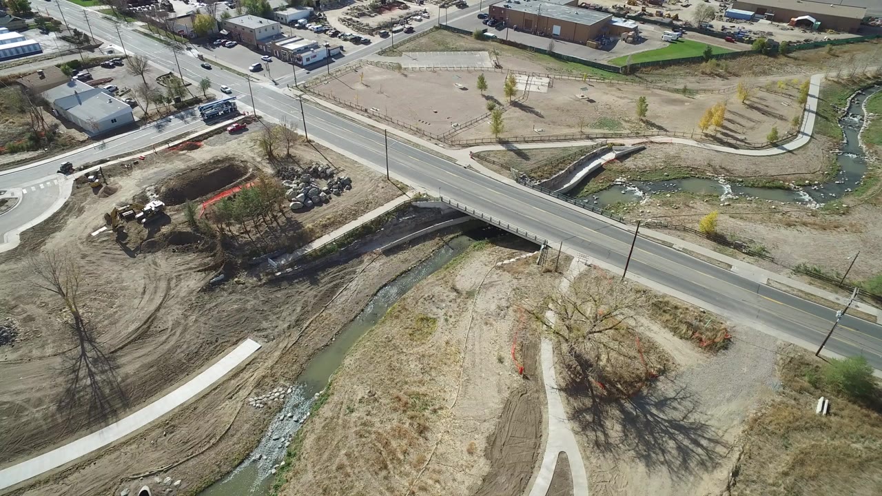 Aerial view of a road crossing a narrow creek near dirt lots and parked cars.