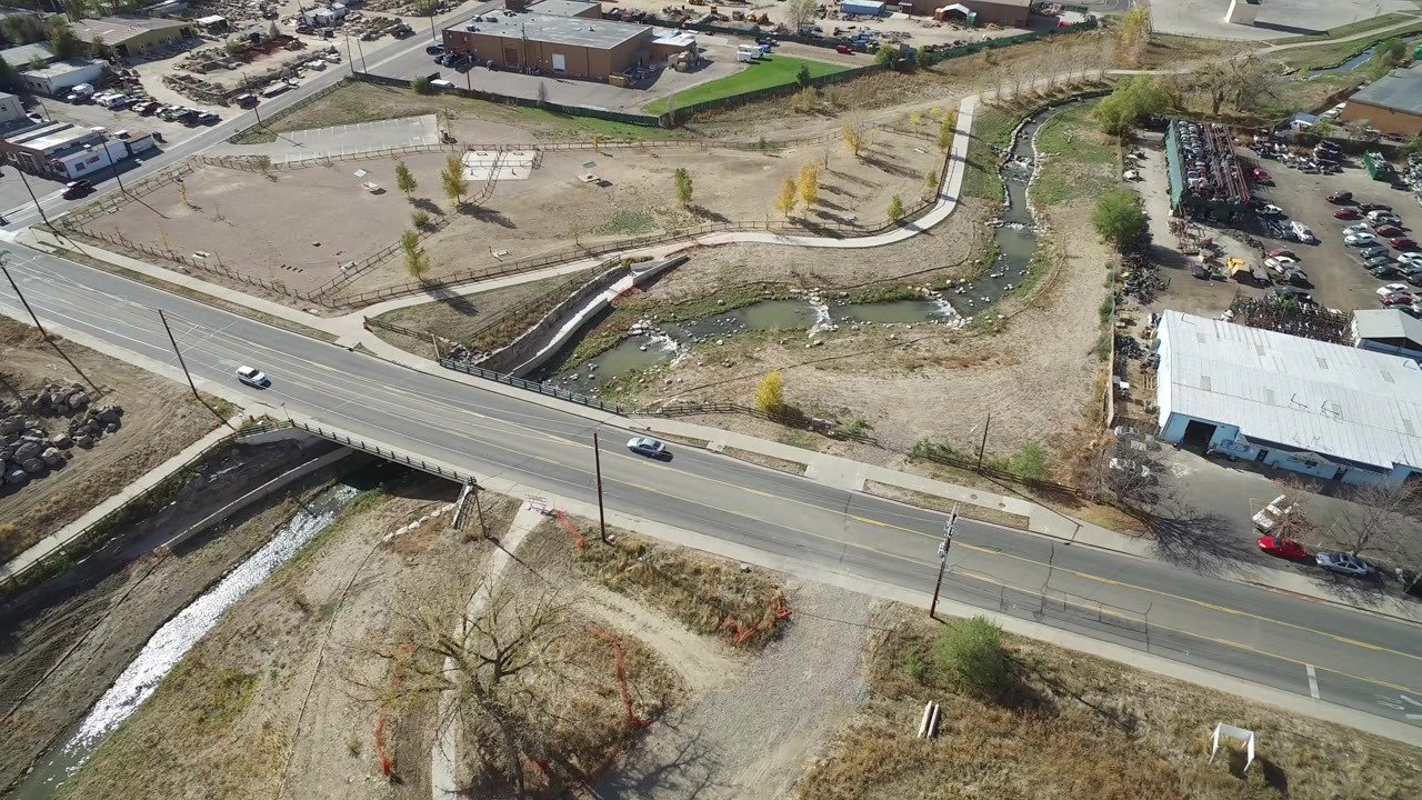 Aerial view of a road, creek channel, dirt lots, and parking areas.