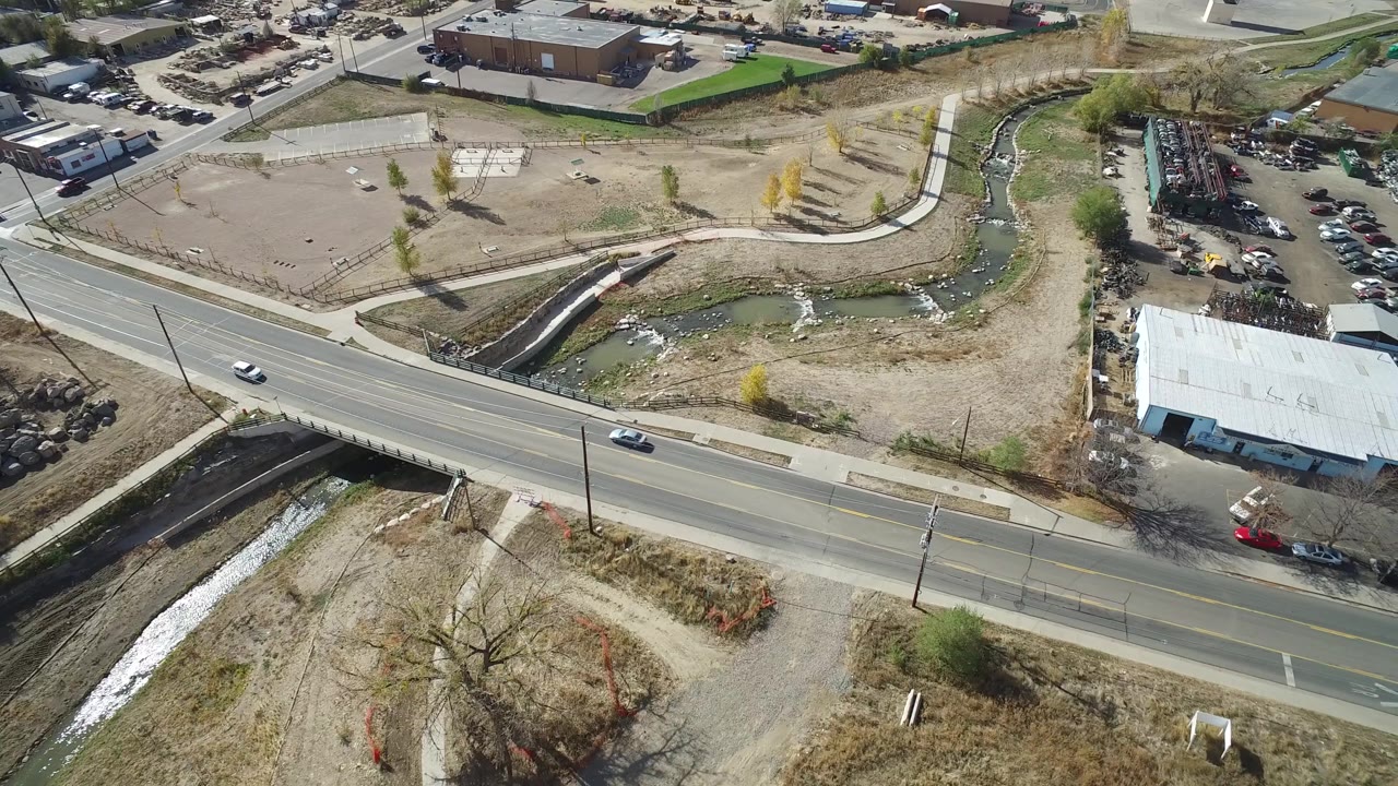 Aerial frame in Hidden Lake, Colorado with the road across the lower frame, cars traveling along it, a narrow water channel, a white-roofed building, parked vehicles, and no visible people.