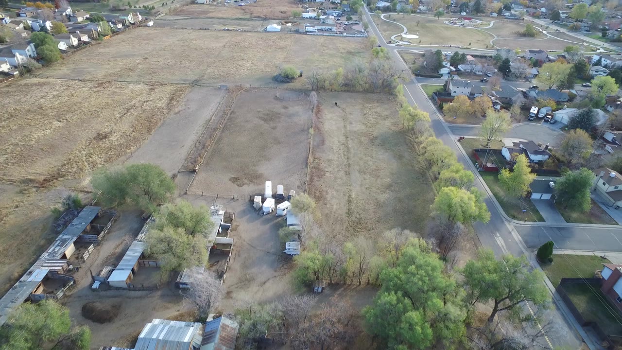 Aerial view of fields, neighborhood roads, trees, and outbuildings.