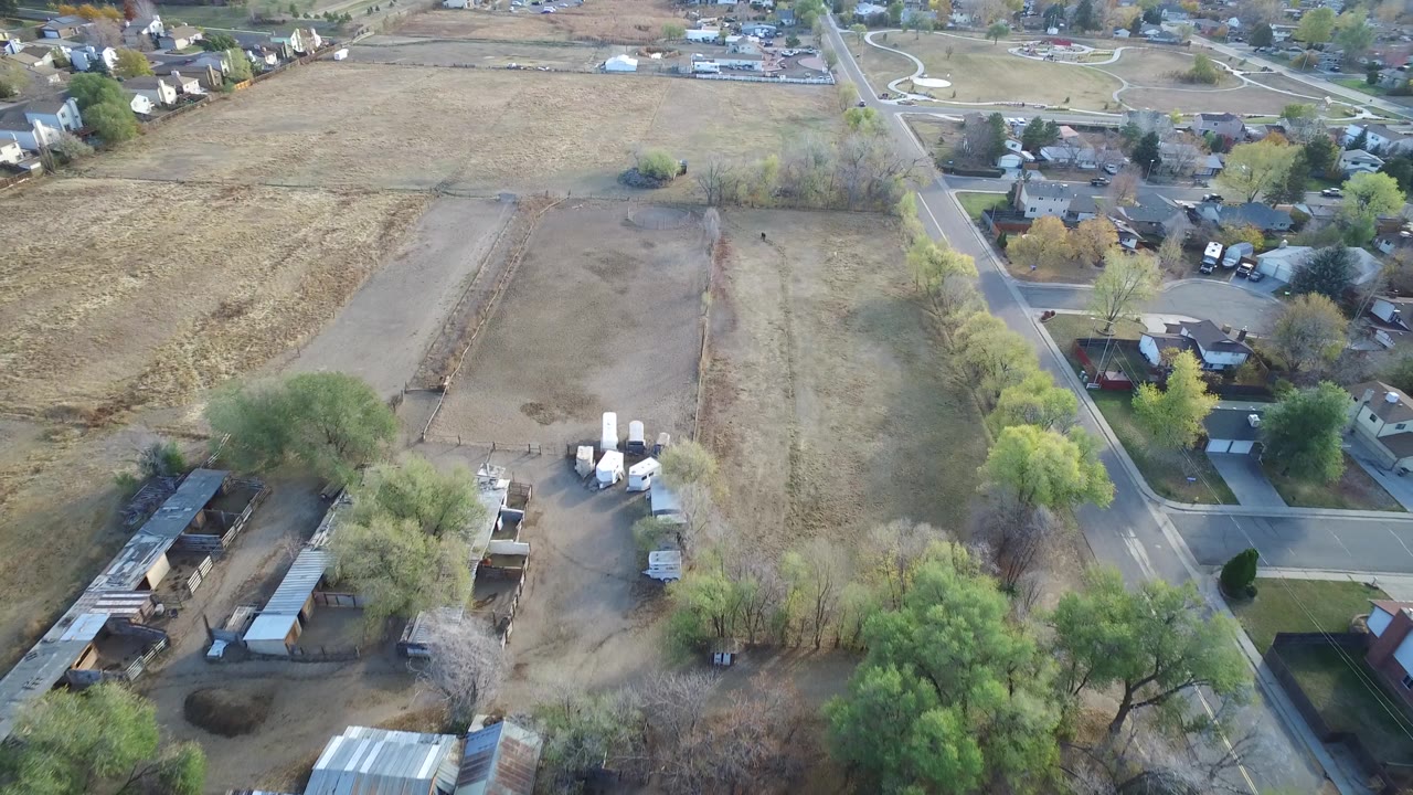 Aerial view in Hidden Lake, Colorado with a brown field in the upper frame, sheds and trees in the lower frame, a road to the right, and no visible people.