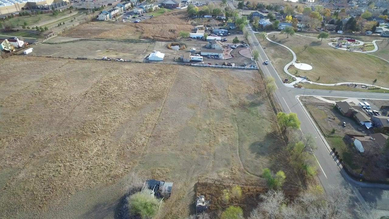 High aerial frame over Hidden Lake, Colorado showing dry open fields, a straight road, houses, trees, and no visible people at the start of the clip.