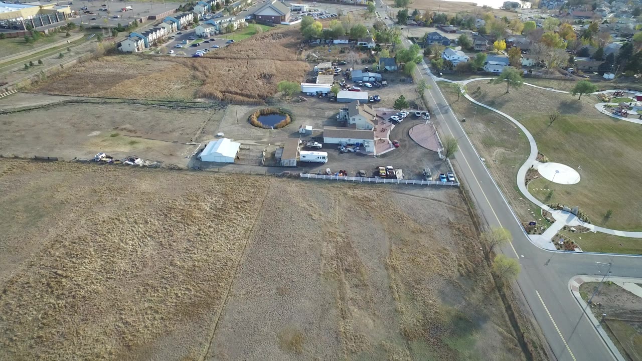 Aerial frame in Hidden Lake, Colorado with the road running vertically near the right side, brown fields across the lower half, and residential buildings and trees across the top.