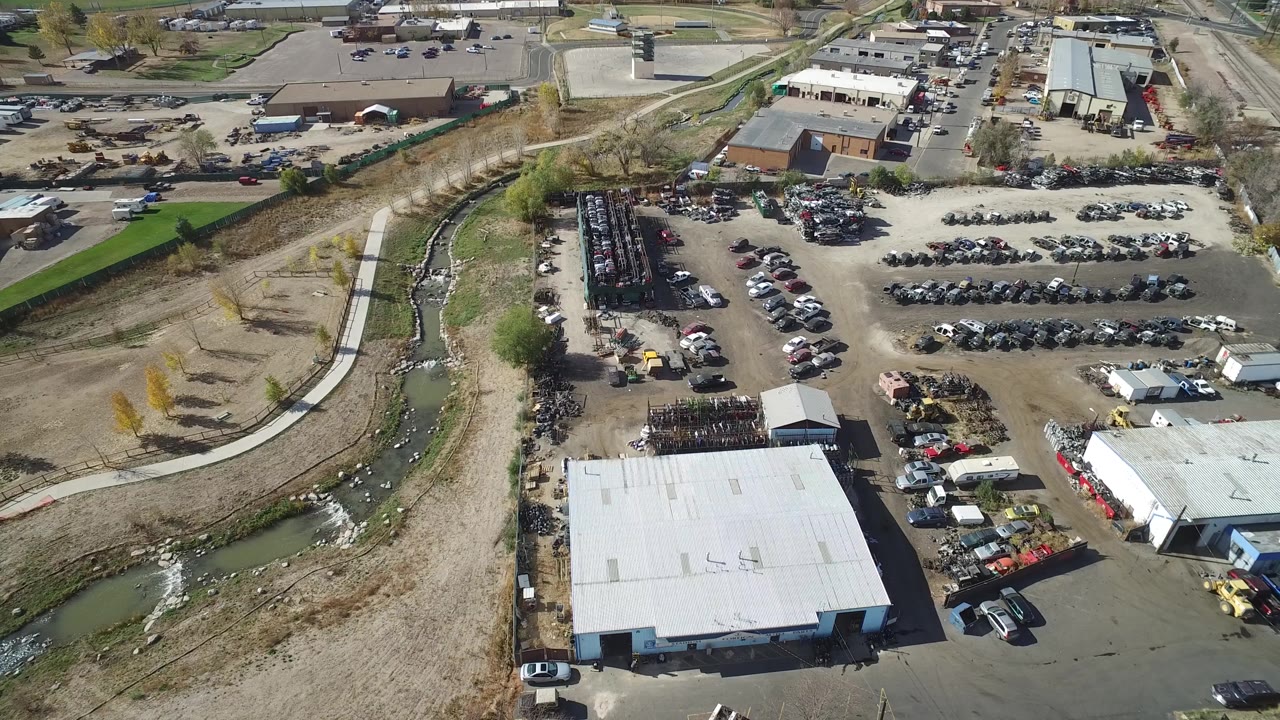 Drone-like view of warehouse roofs, car rows, equipment areas, and a river corridor.