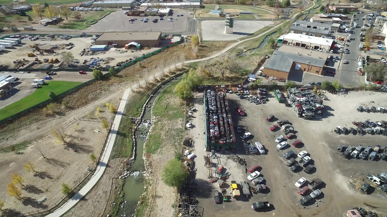 Oblique aerial view over industrial buildings, car rows, parking lots, and open dry ground.