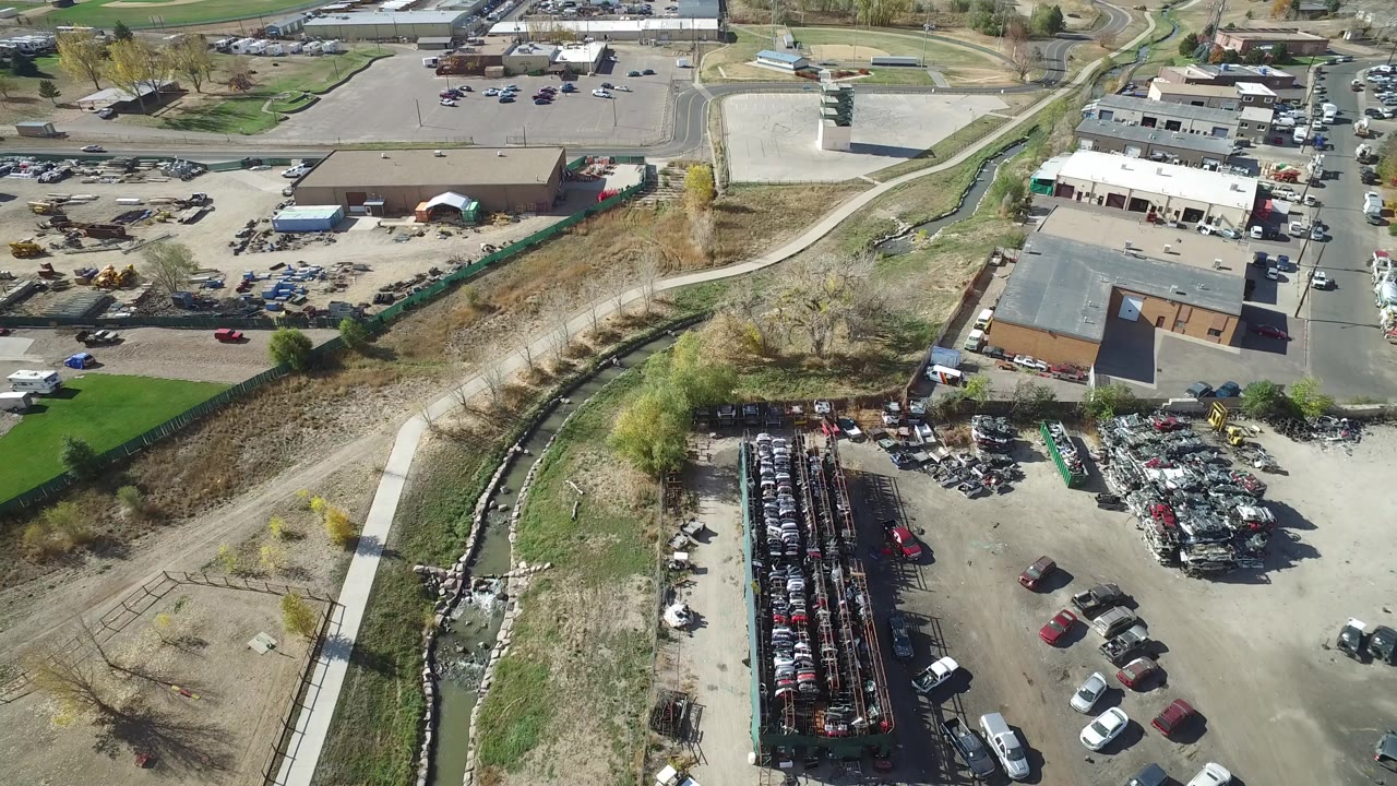 Aerial view of industrial lots, parked vehicles, buildings, and a drainage corridor.