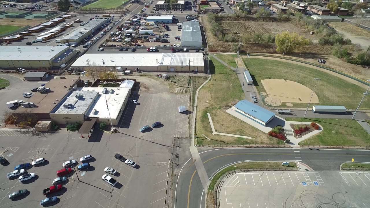 Aerial view of commercial buildings, parking lots, road, grass, and baseball field.