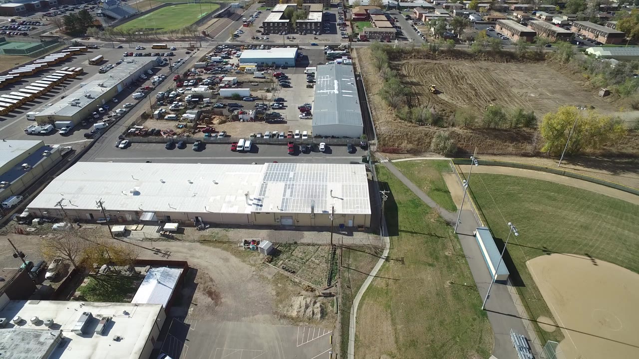 Aerial view of industrial buildings, parking lots, sports fields, and open dirt land.