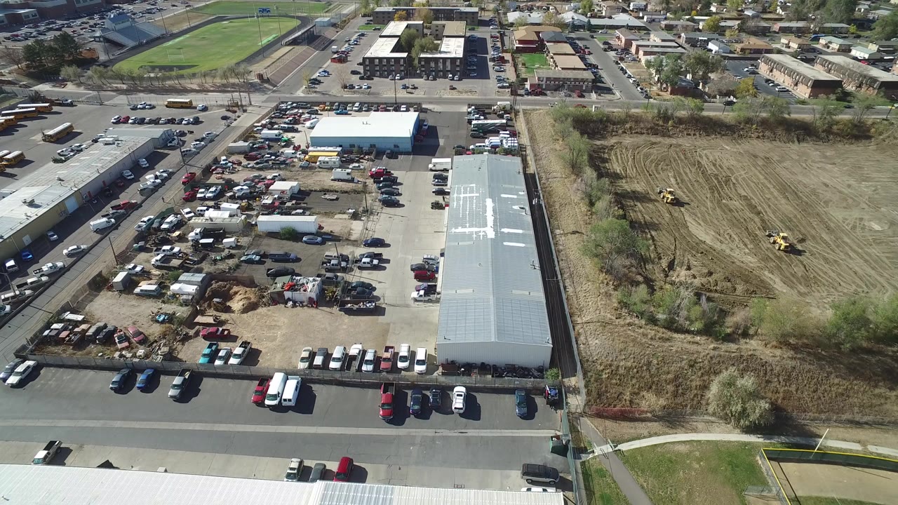 Aerial view of a road, warehouse lot, parked vehicles, and a cleared field.