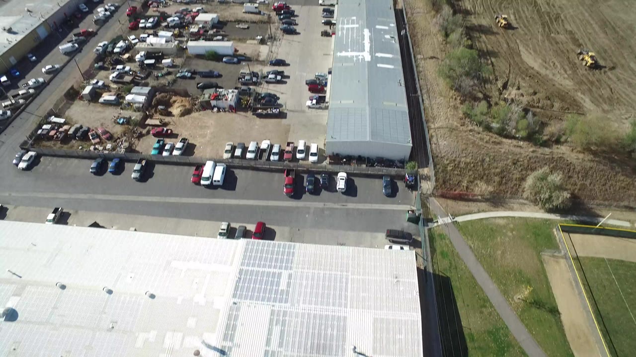 Aerial frame in Hidden Lake, Colorado, showing the edge of a large white-roofed building, parked vehicles along a road, open lots, and no visible people.