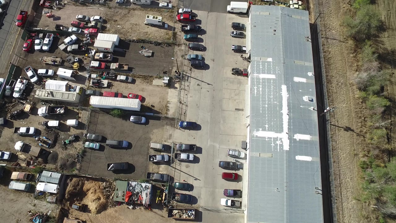 First frame of the Hidden Lake, Colorado aerial shows a full vehicle lot, trailers, a paved drive, a long pale roof, rail tracks, dry grass, and no visible people.